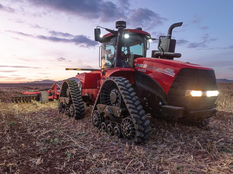 A 执行官® tractor that's towing tilling equipment across a field at sunrise